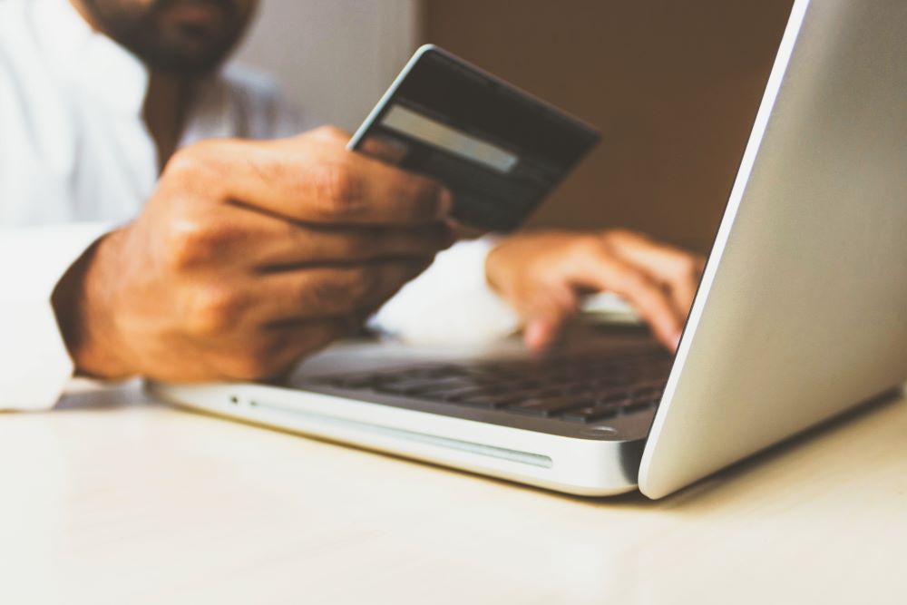 Close up of a hand holding a credit card in one hand and typing on a laptop with the other.